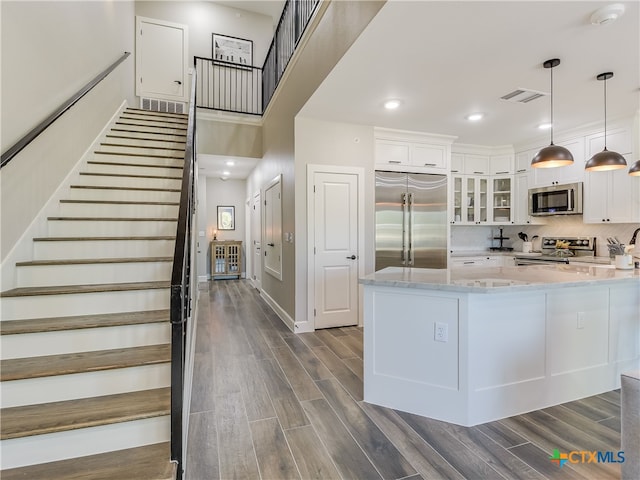 kitchen with stainless steel appliances, white cabinetry, light stone countertops, dark hardwood / wood-style floors, and hanging light fixtures