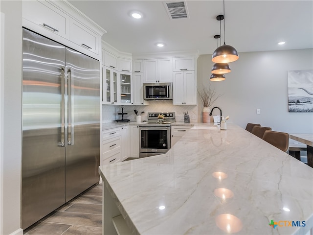 kitchen with light stone counters, stainless steel appliances, hanging light fixtures, sink, and white cabinets