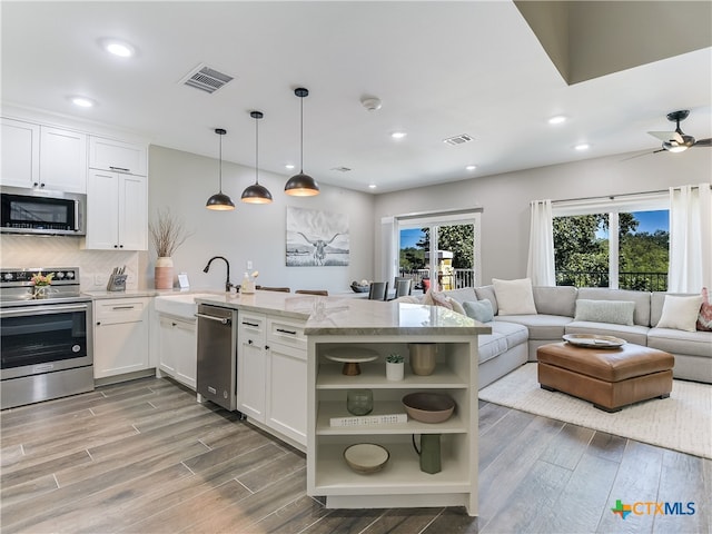 kitchen featuring kitchen peninsula, appliances with stainless steel finishes, hanging light fixtures, and white cabinets