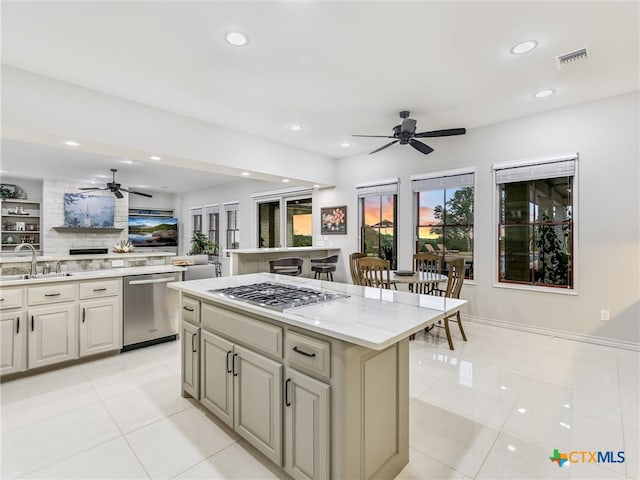 kitchen featuring stainless steel appliances, light tile patterned flooring, sink, light stone counters, and a kitchen island