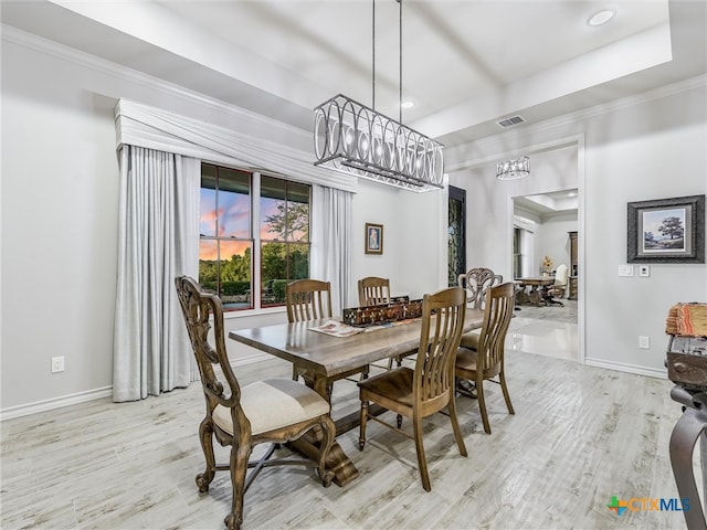 dining space featuring a tray ceiling, ornamental molding, and light hardwood / wood-style flooring