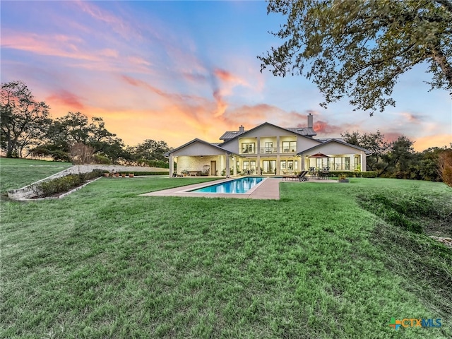 pool at dusk featuring a patio and a lawn