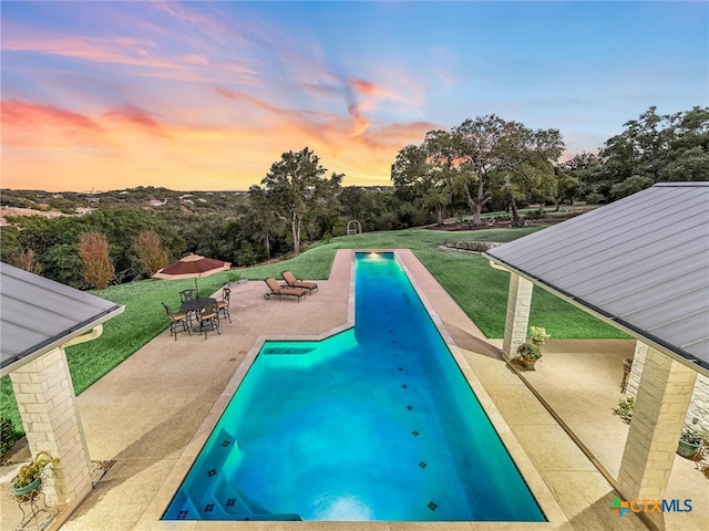 pool at dusk with a yard and a patio