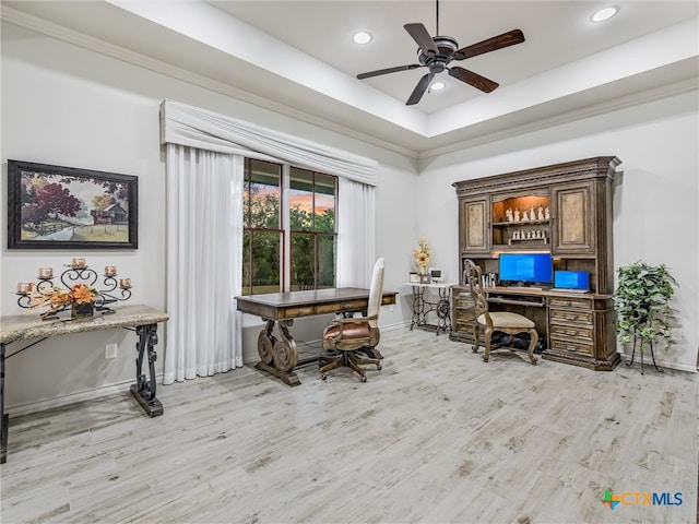 home office featuring ceiling fan, light hardwood / wood-style flooring, and a tray ceiling