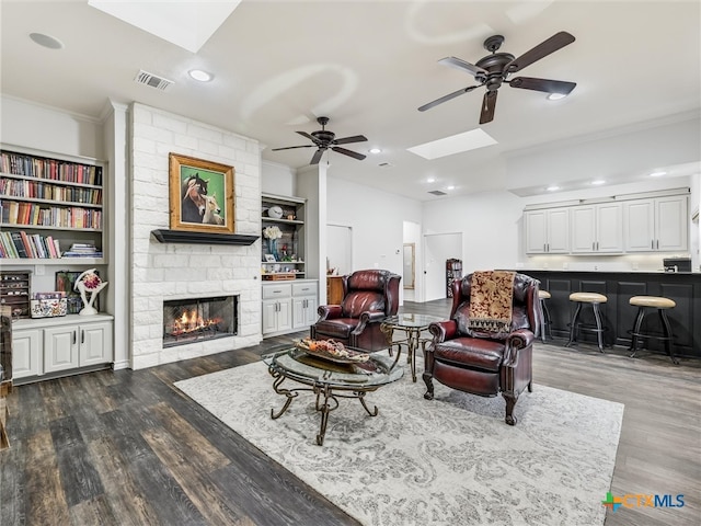 living room featuring a stone fireplace, dark hardwood / wood-style flooring, ceiling fan, and crown molding