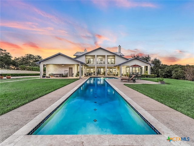 pool at dusk featuring a patio and a yard