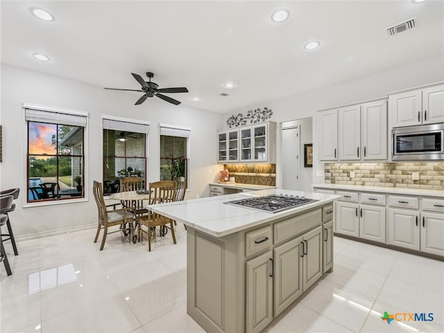 kitchen with backsplash, light tile patterned floors, a kitchen island, and appliances with stainless steel finishes