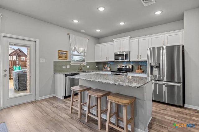 kitchen with visible vents, a sink, a center island, appliances with stainless steel finishes, and decorative backsplash