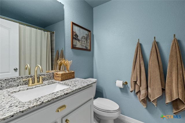 full bathroom with vanity, toilet, a textured wall, and baseboards