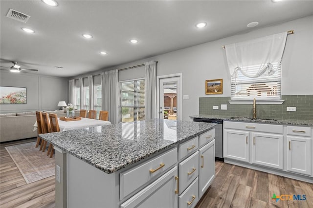 kitchen with visible vents, a sink, stainless steel dishwasher, wood finished floors, and a center island