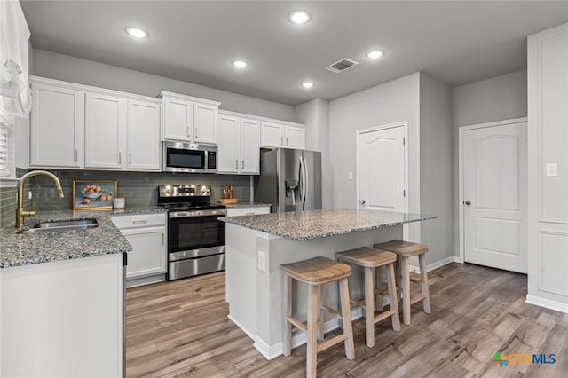 kitchen with appliances with stainless steel finishes, a sink, a center island, backsplash, and light wood-style floors