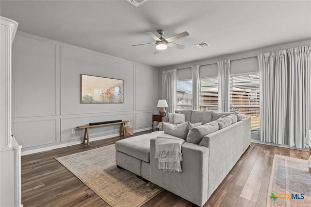 living area with ceiling fan, visible vents, dark wood finished floors, and a decorative wall