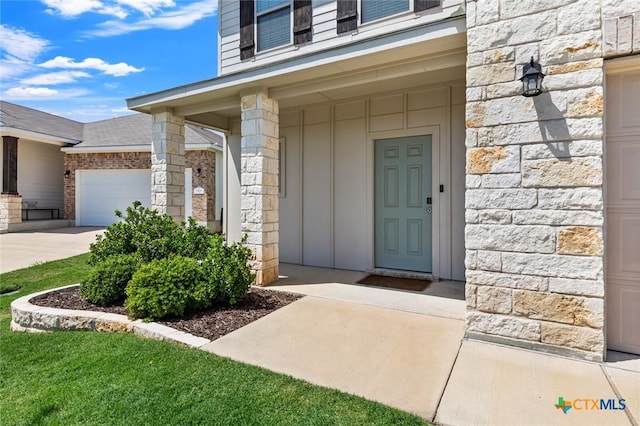 entrance to property with stone siding, an attached garage, board and batten siding, and driveway
