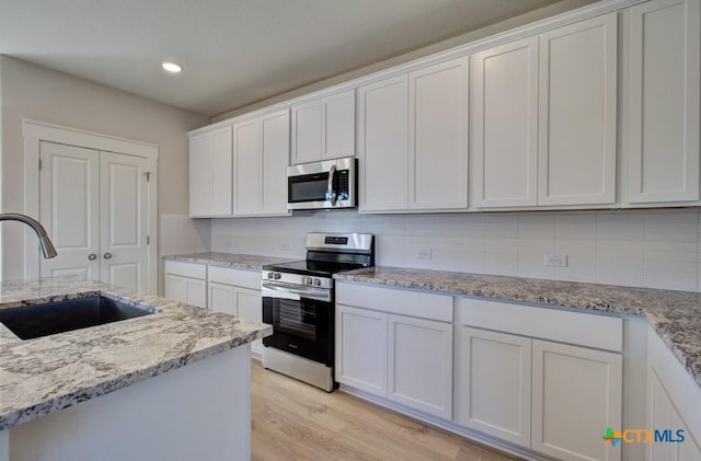 kitchen with light stone countertops, stainless steel appliances, white cabinetry, and sink