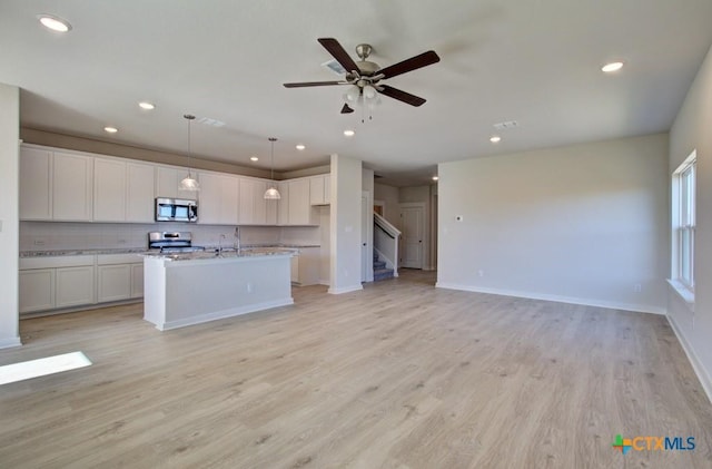 kitchen with light stone countertops, stainless steel appliances, decorative light fixtures, a center island with sink, and white cabinets