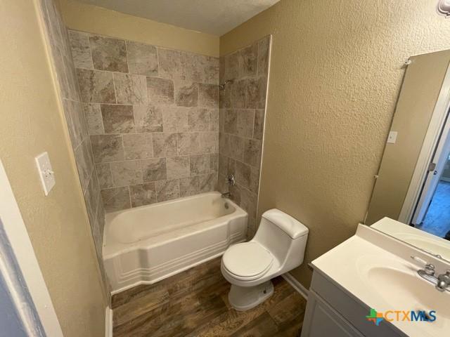 full bathroom with toilet, tiled shower / bath, wood-type flooring, and vanity