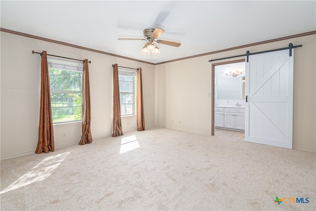 carpeted spare room featuring ornamental molding, a barn door, and ceiling fan