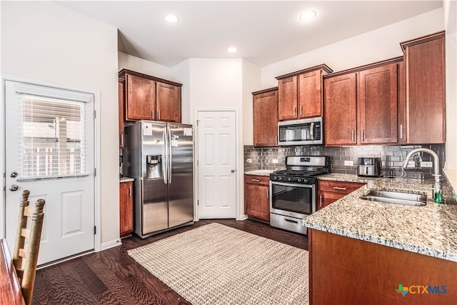 kitchen featuring stainless steel appliances, dark hardwood / wood-style flooring, light stone counters, sink, and tasteful backsplash