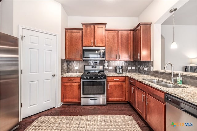 kitchen featuring sink, light stone counters, appliances with stainless steel finishes, hanging light fixtures, and dark wood-type flooring