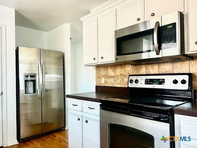 kitchen with a textured ceiling, appliances with stainless steel finishes, white cabinetry, decorative backsplash, and light hardwood / wood-style flooring