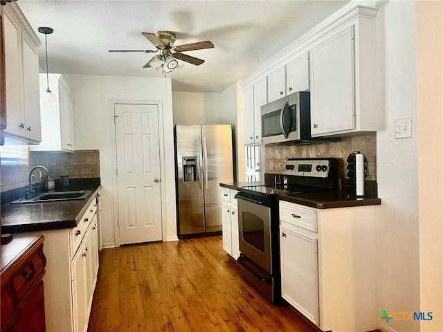 kitchen with hanging light fixtures, appliances with stainless steel finishes, sink, white cabinets, and light wood-type flooring