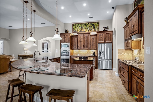 kitchen featuring arched walkways, a spacious island, appliances with stainless steel finishes, a kitchen bar, and a sink