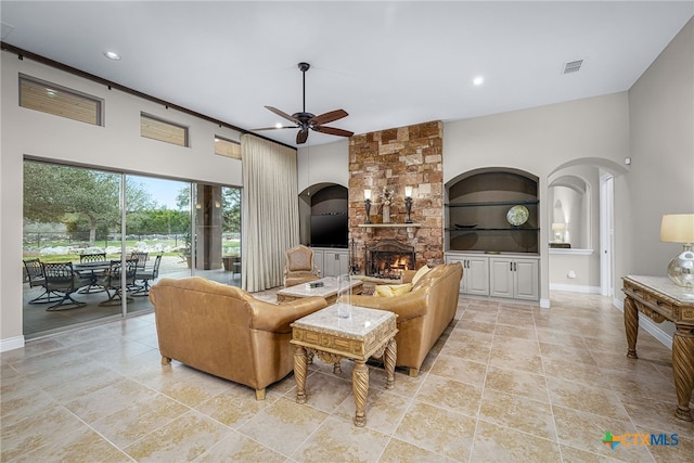 living area with visible vents, arched walkways, a ceiling fan, built in shelves, and a fireplace