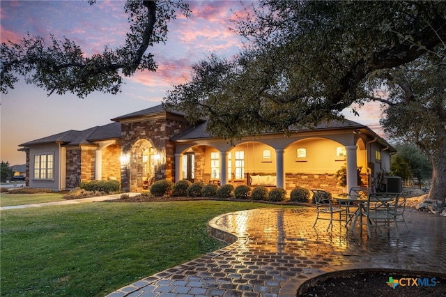 mediterranean / spanish home with central air condition unit, stone siding, a patio area, and a lawn