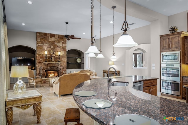 kitchen featuring visible vents, appliances with stainless steel finishes, dark stone countertops, a stone fireplace, and a sink