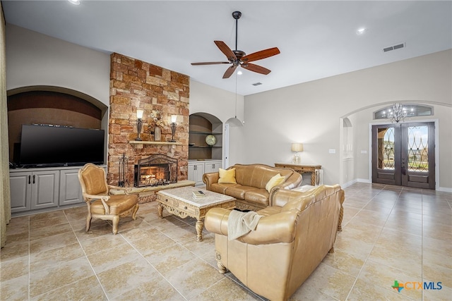 living area featuring arched walkways, a fireplace, visible vents, a ceiling fan, and french doors