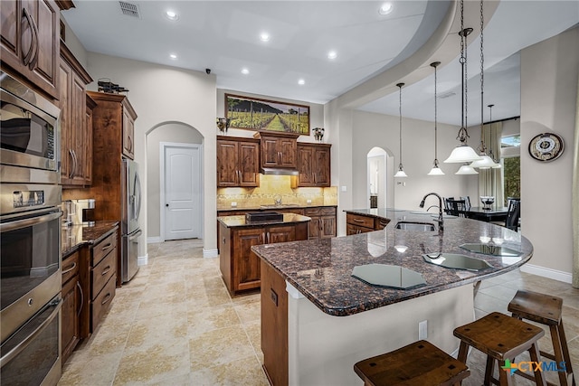 kitchen with arched walkways, a spacious island, stainless steel appliances, visible vents, and a sink