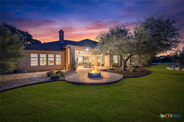 back of house at dusk with a yard, an outdoor fire pit, a patio, and stucco siding