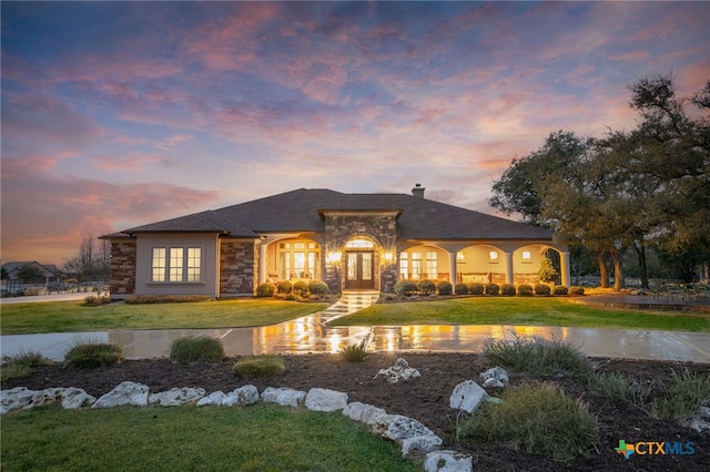 view of front of home featuring stone siding, french doors, a chimney, and a front yard