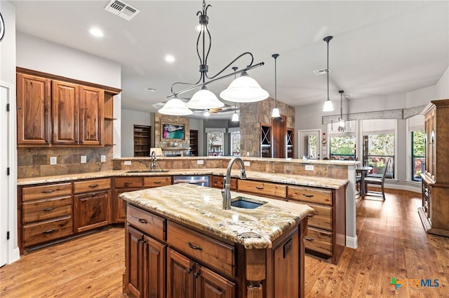 2299 Sun Chase Blvd, New Braunfels, TX 78130 - kitchen with a peninsula, a kitchen island with sink, tasteful backsplash, light wood-style floors, and light stone counters