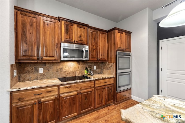 2299 Sun Chase Blvd, New Braunfels, TX 78130 - kitchen featuring stainless steel appliances, light wood-style flooring, decorative backsplash, light stone counters, and brown cabinetry