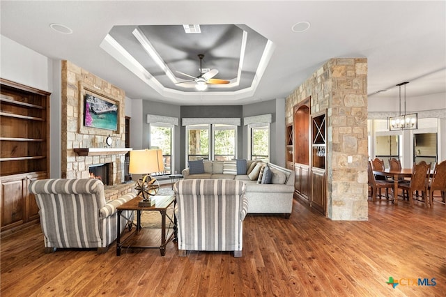 2299 Sun Chase Blvd, New Braunfels, TX 78130 - living area with ceiling fan, a tray ceiling, a fireplace, wood finished floors, and a chandelier