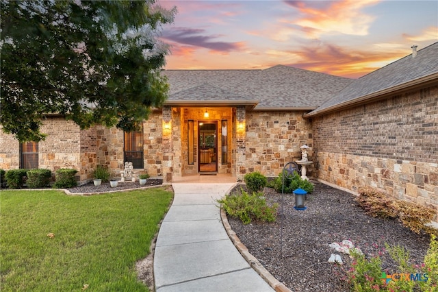2299 Sun Chase Blvd, New Braunfels, TX 78130 - exterior entry at dusk with a lawn, roof with shingles, and stone siding