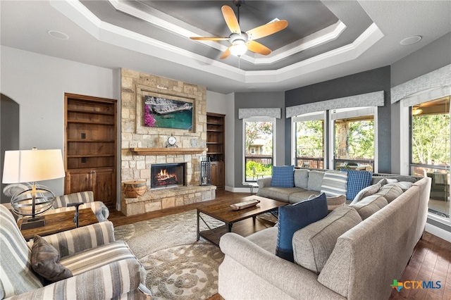 2299 Sun Chase Blvd, New Braunfels, TX 78130 - living room featuring a raised ceiling, ceiling fan, wood-type flooring, a stone fireplace, and ornamental molding