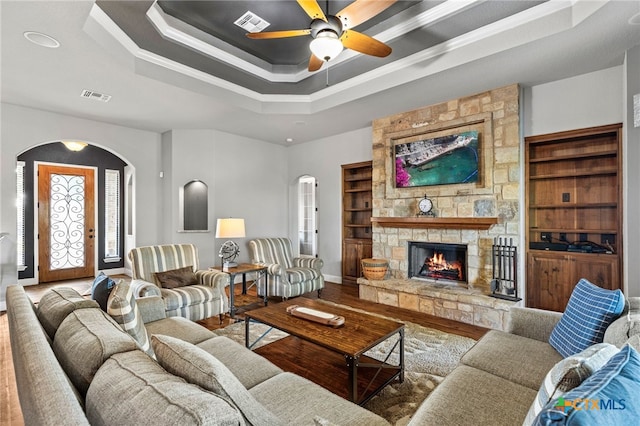 2299 Sun Chase Blvd, New Braunfels, TX 78130 - living room with arched walkways, wood finished floors, a tray ceiling, a ceiling fan, and a fireplace