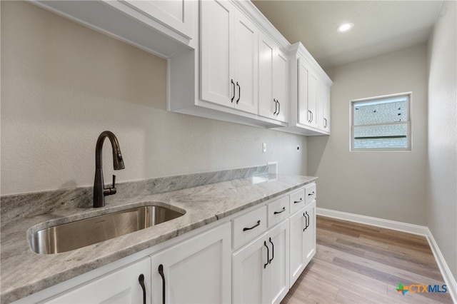 kitchen with light hardwood / wood-style flooring, sink, light stone counters, and white cabinets