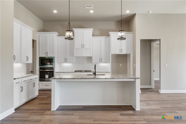 kitchen with white cabinetry, appliances with stainless steel finishes, decorative light fixtures, and a kitchen island with sink