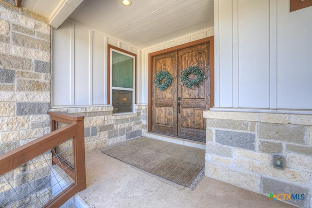 doorway to property with stone siding, board and batten siding, and covered porch