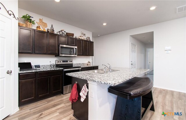 348 Jacquard Ct, Troy, TX 76579 - kitchen with light wood-type flooring, appliances with stainless steel finishes, dark brown cabinetry, sink, and a kitchen island with sink