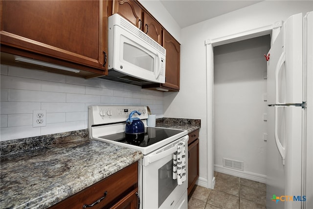 kitchen with tasteful backsplash, white appliances, dark stone counters, and light tile patterned floors