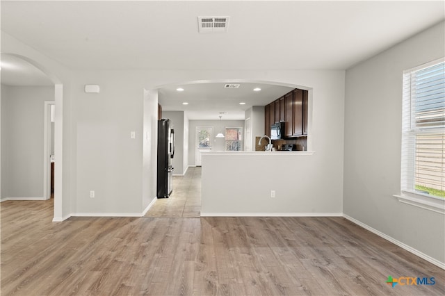 unfurnished living room with plenty of natural light, sink, and light hardwood / wood-style flooring