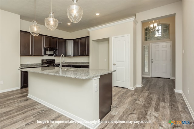 kitchen featuring hardwood / wood-style floors, black appliances, an island with sink, and light stone countertops