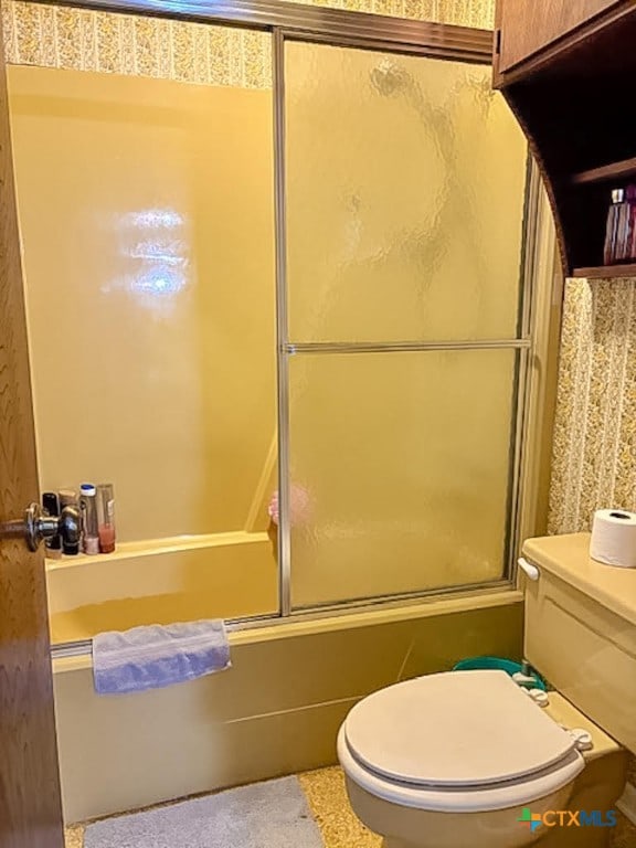 bathroom featuring toilet and combined bath / shower with glass door