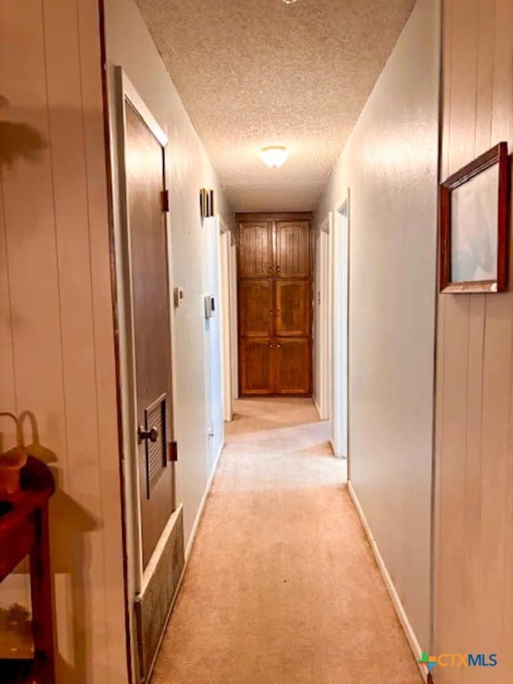 hallway with a textured ceiling and light carpet