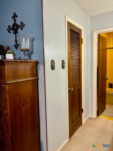 hallway featuring light colored carpet and a textured ceiling