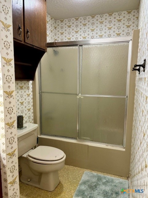 bathroom featuring bath / shower combo with glass door, a textured ceiling, and toilet